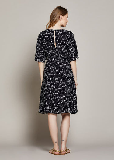 Pregnant Woman wearing a black polka dot dress on a plain background